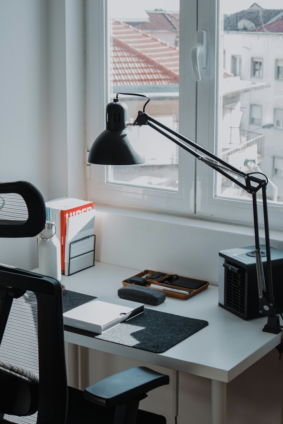Ein aufgeräumter Schreibtisch im Heimbüro mit Büromaterial neben einem Fenster.